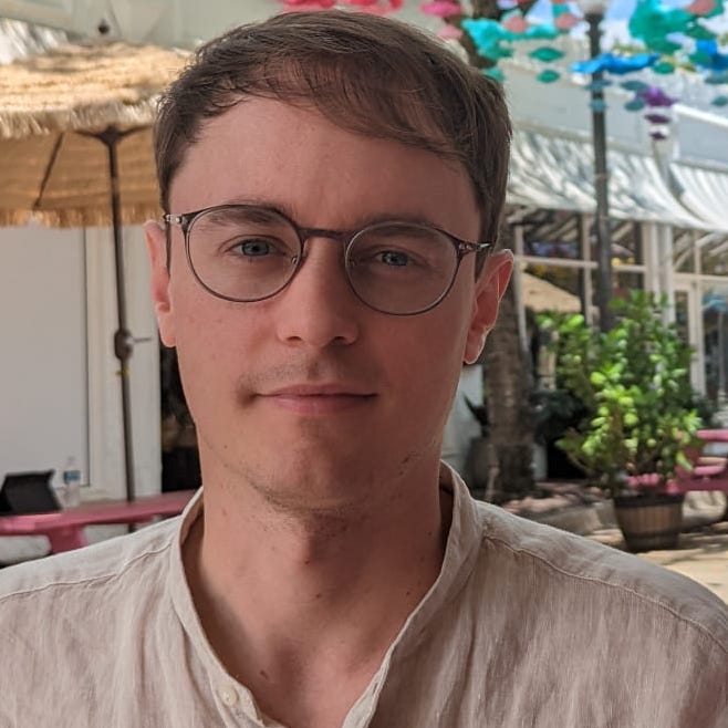 White male wearing glasses, in white shirt, with colourful background.