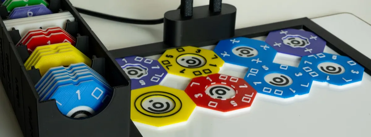 Colourful octagonal programming tiles with raised symbols arranged on a white board, next to a tray of spare tiles.